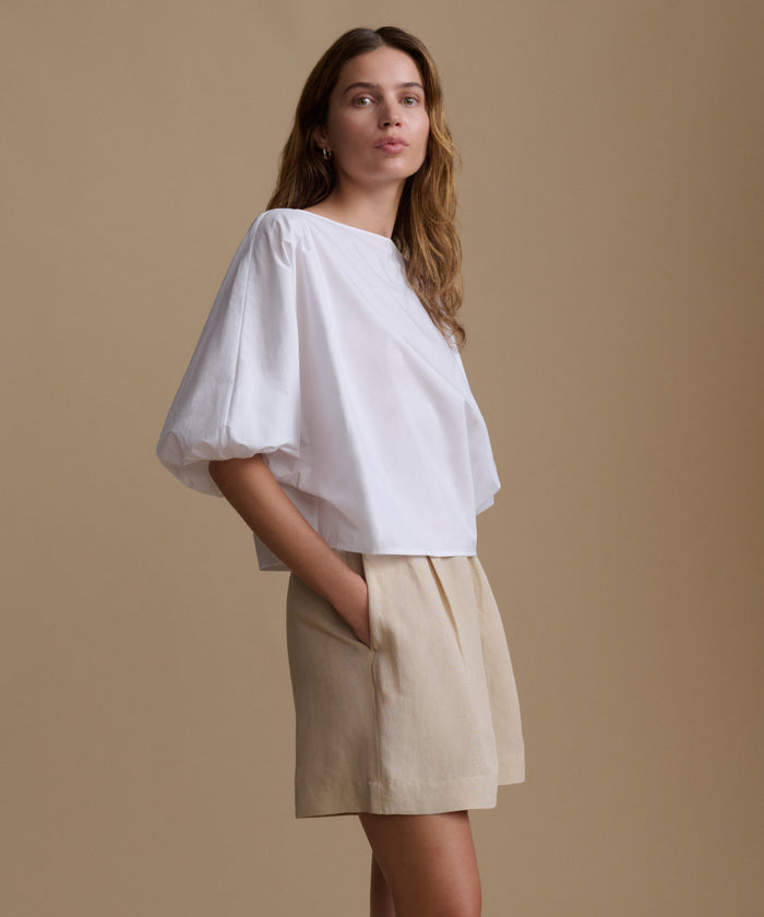Woman wearing a white blouse and beige shorts against a beige background.