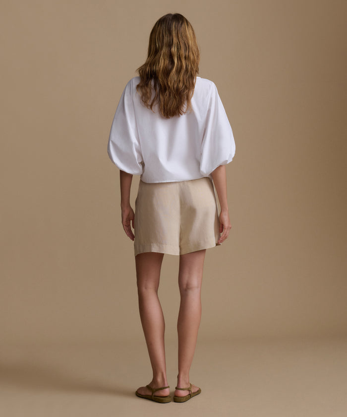 Woman wearing a white blouse and beige shorts against a beige background.