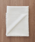 A Frayed Linen Tablecloth, crafted from 100% linen with stylish frayed edges, is elegantly displayed on a wooden surface.