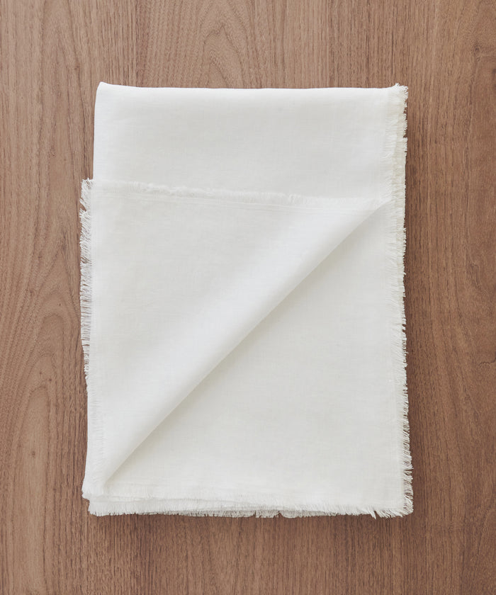 A Frayed Linen Tablecloth, crafted from 100% linen with stylish frayed edges, is elegantly displayed on a wooden surface.
