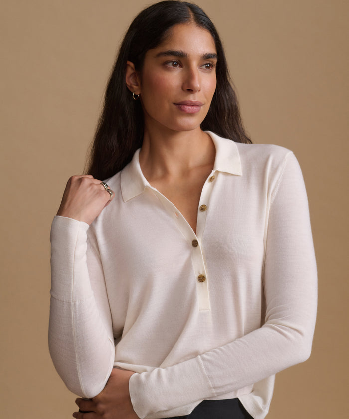 A woman modeling a long-sleeve cream knit polo shirt with a buttoned collar, posed against a solid beige studio background.