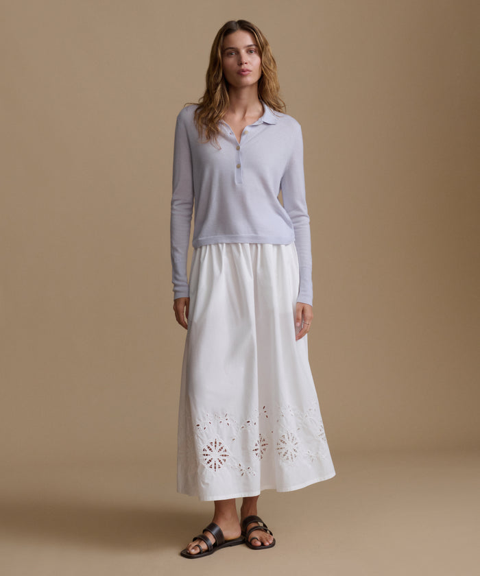 Woman wearing a light blue long-sleeve top and white skirt with cut-out patterns on a beige background