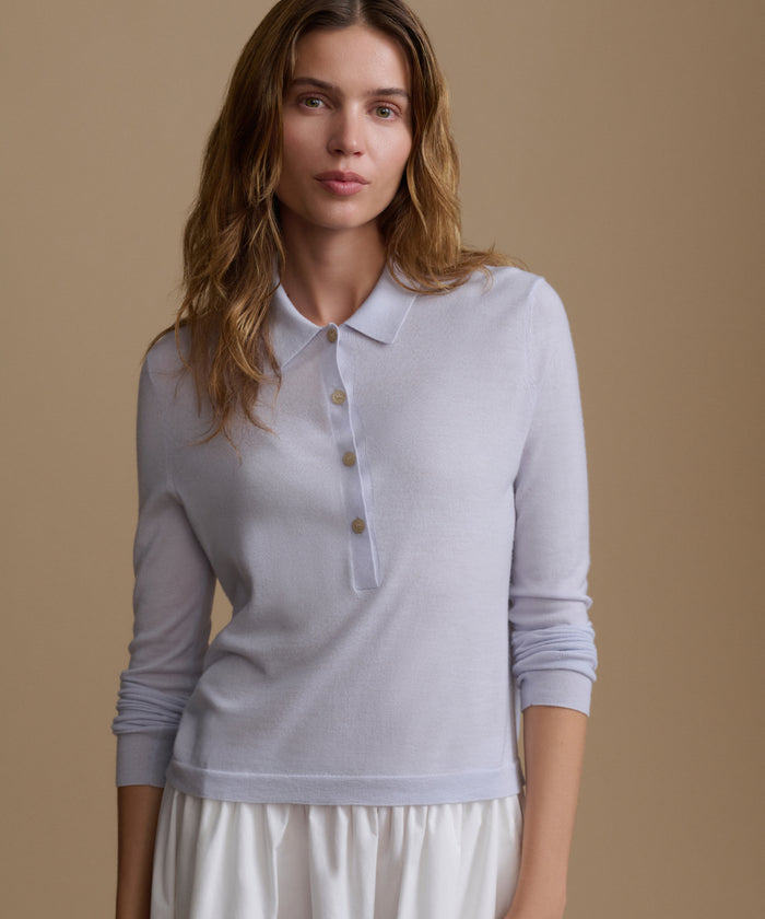 Woman wearing a light blue long-sleeve top and white skirt with white skirt on a beige background.