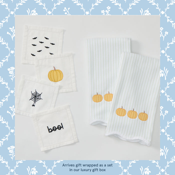 A set of white Halloween-themed baby textiles, including two ribbed square cloths with embroidered pumpkins and three smaller square cloths with embroidered bats, a spider web, and the word 'boof!' in black, displayed on a white background with a blue floral border.