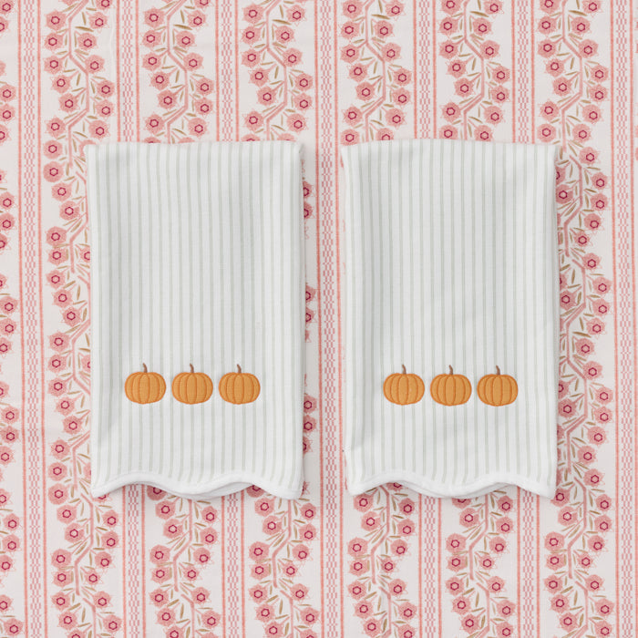Two white ribbed baby blankets with embroidered orange pumpkins, laid flat on a pink and white patterned fabric background.