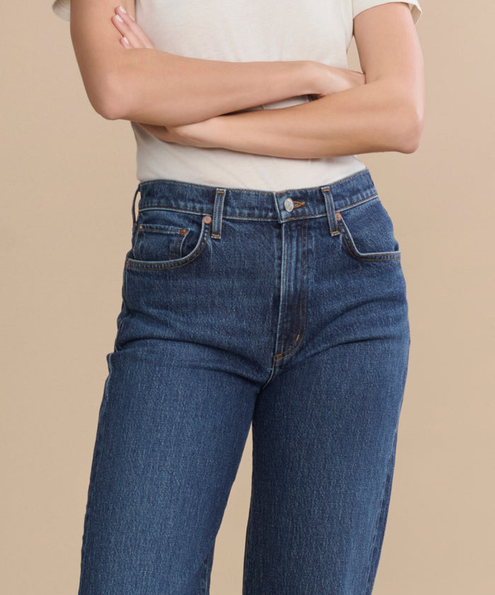 A person in a white short-sleeve shirt and Harper Jean—a relaxed mid-rise, wide-leg style—stands with arms crossed against a plain beige background.