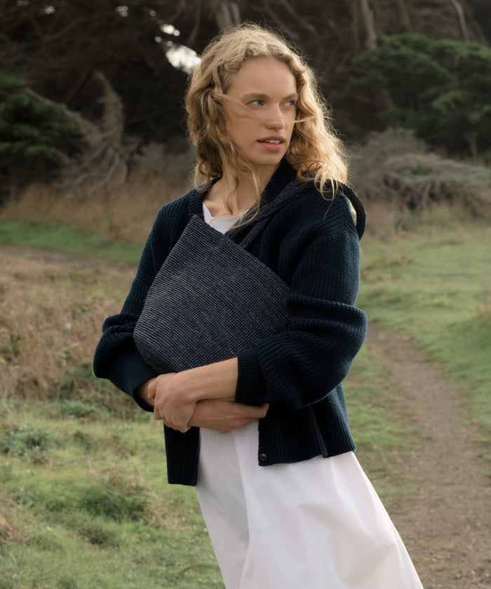 Woman holding a navy hollis bag outdoors in a natural setting