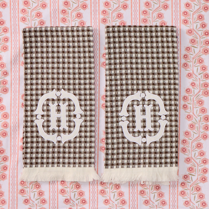 Two folded brown and cream gingham towels with white fringed edges, each featuring a large white embroidered 'H' monogram.