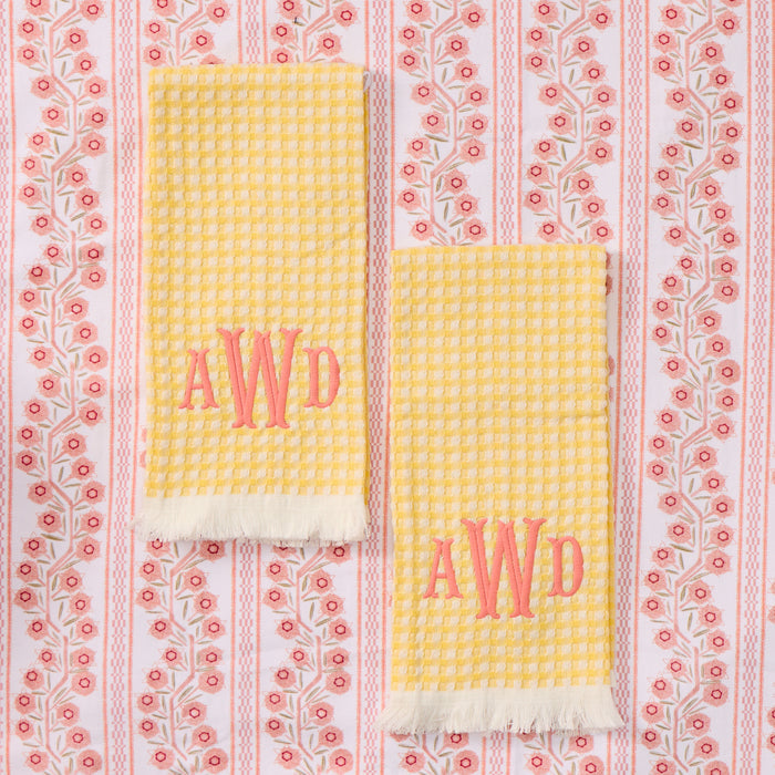 Two folded yellow and white gingham towels with white fringed edges, each featuring a large red embroidered 'AWD' monogram.