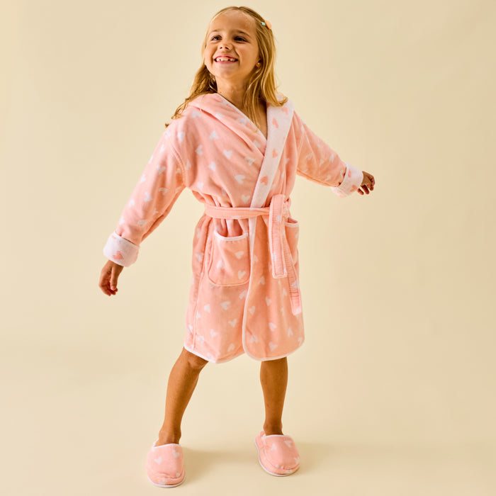 Smiling girl wearing a fluffy coral pink bathrobe with white hearts and matching slippers.