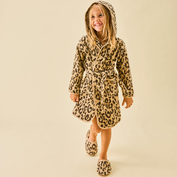 A smiling girl wearing a fluffy leopard print hooded bathrobe and matching slippers.