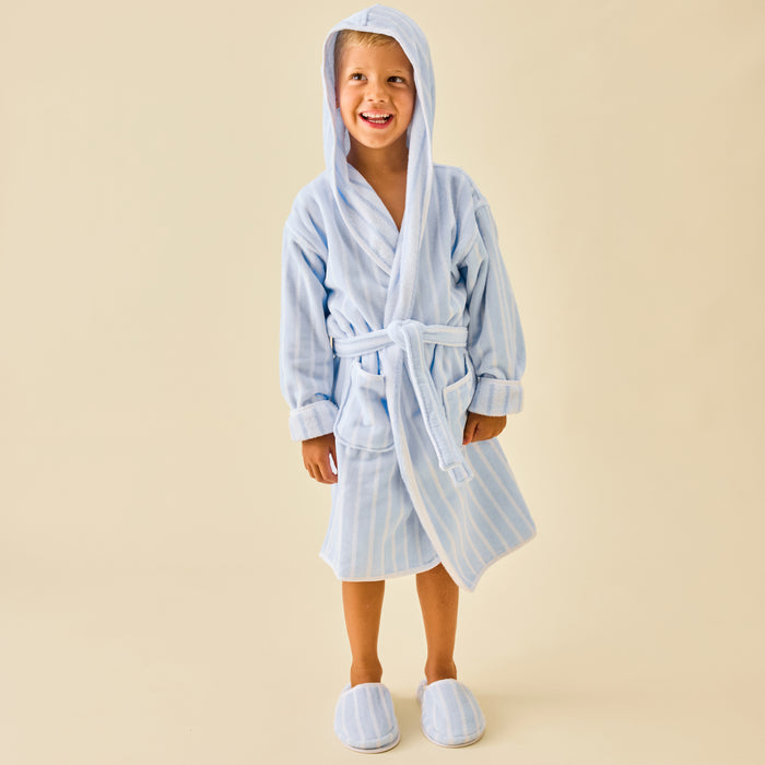 Smiling boy wearing a fluffy light blue striped bathrobe and matching slippers.
