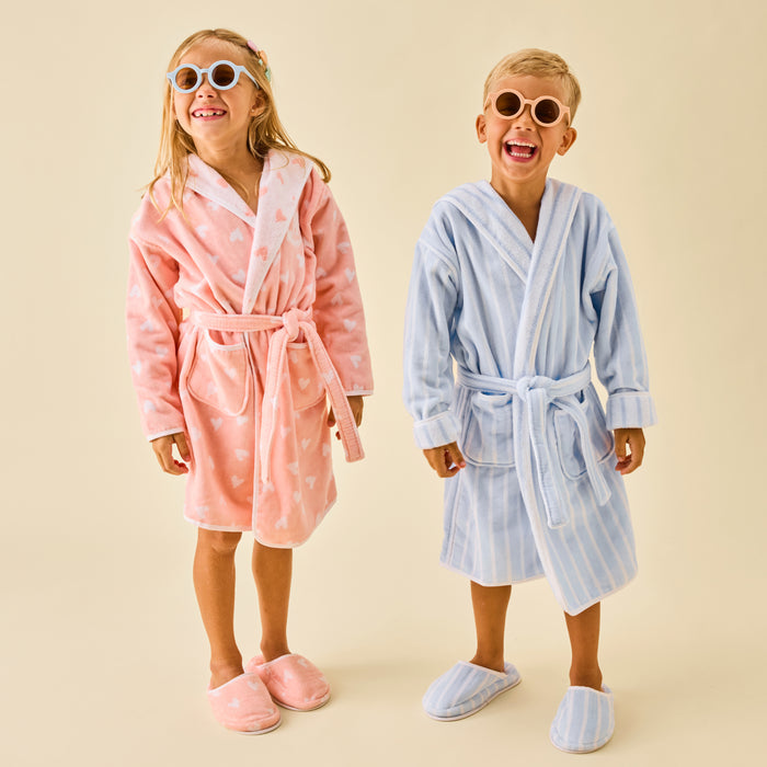 Two kids smiling in Coral Hearts and Light Blue Stripe bathrobes with matching slippers.