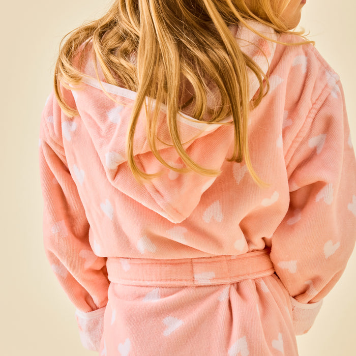 A girl wearing fluffy coral pink bathrobe with white hearts.