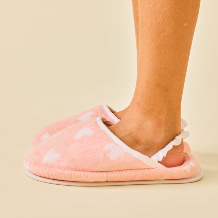 Child's feet wearing fluffy coral pink slippers with white hearts and a ruffled elastic strap.