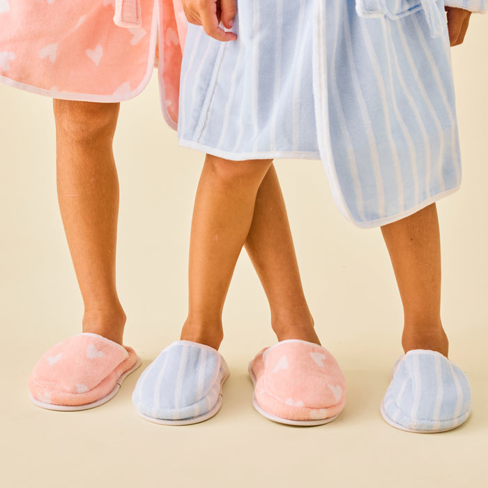 Two kids wearing soft terry slippers and matching bathrobes in coral hearts and blue stripes.