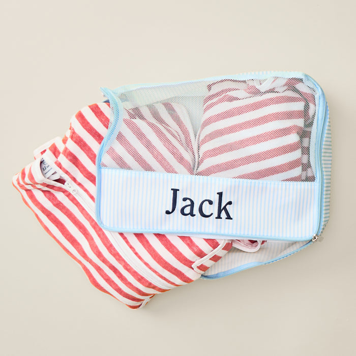 Heritage Blue Stripe packing cube embroidered with 'Jack,' filled with neatly folded red and white striped garments.