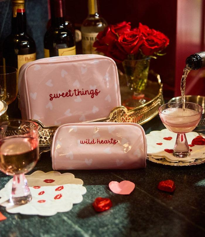 photo of the large and mini patterned toiletry bags archive in Tossed Pink Hearts, wth wine glasses in the background