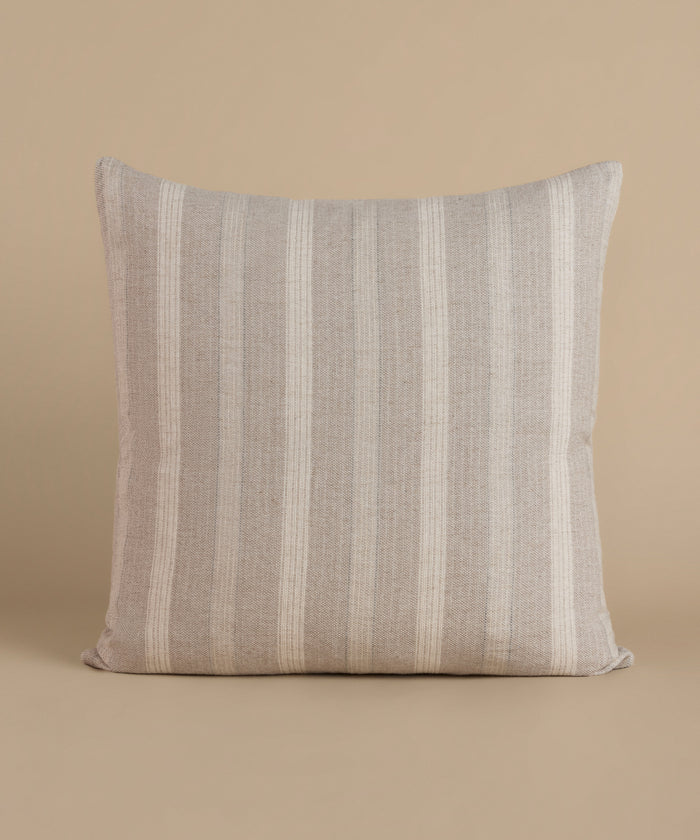 A cream and natural stripe pillow against a beige background.