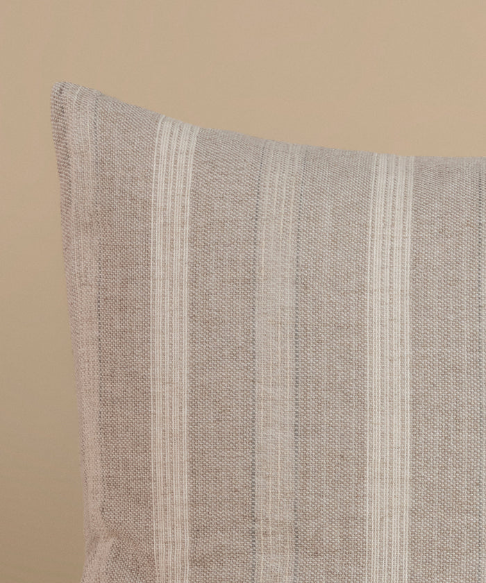 A cream and natural stripe pillow against a beige background.