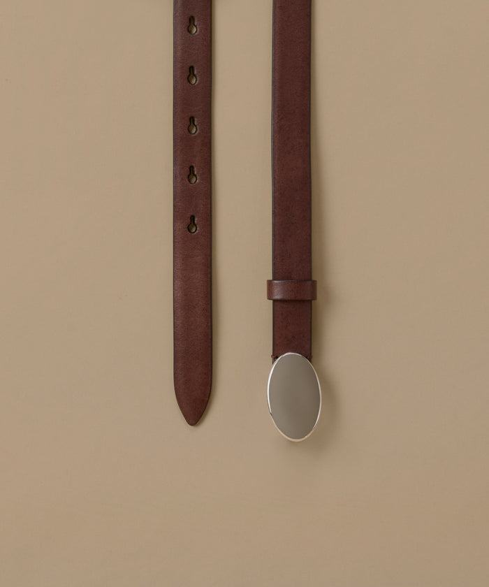 A dark brown leather belt with an oval silver-toned metal buckle, shown hanging vertically against a solid beige background.