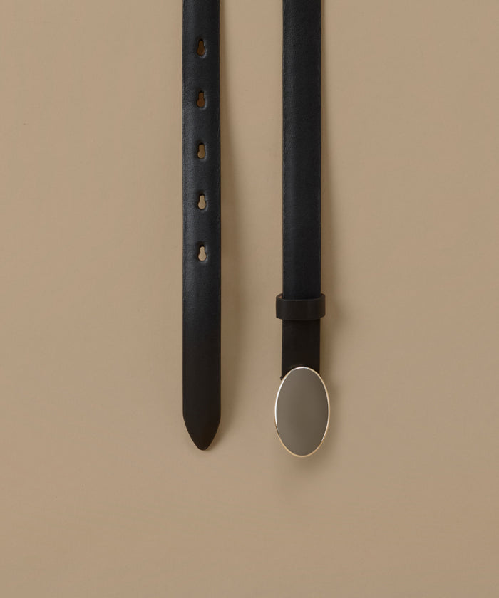 A black leather belt laid flat on a warm beige background, showing the strap with adjustment holes on one side and the buckle on the other. The buckle is a large, polished oval with a silver-toned metal border.