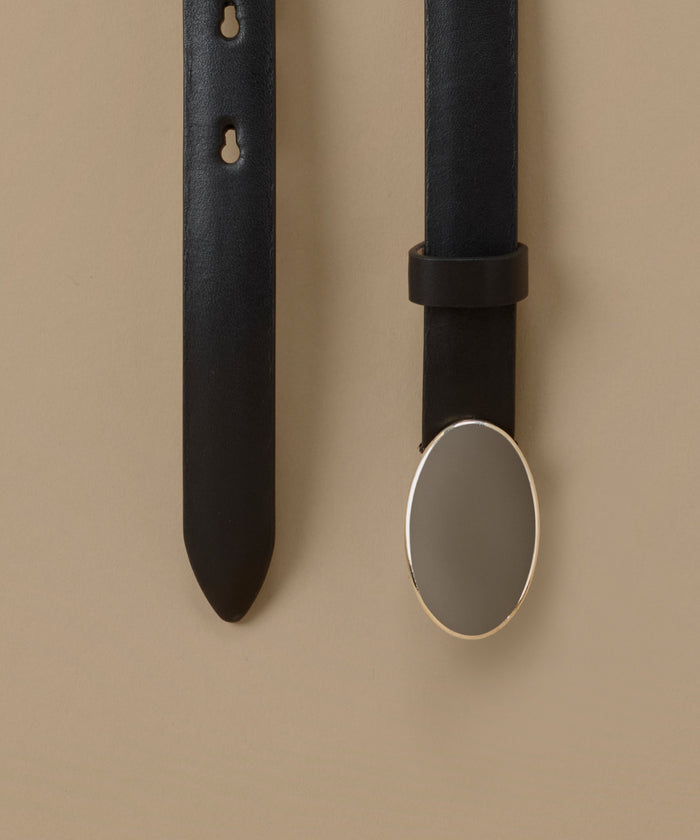 A close-up of a black leather belt shown against a warm beige background, with one vertical strap on the left and another on the right featuring a large oval silver-toned metal buckle.