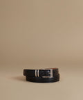 A black leather belt with a silver-tone buckle, neatly coiled on a warm beige studio background.