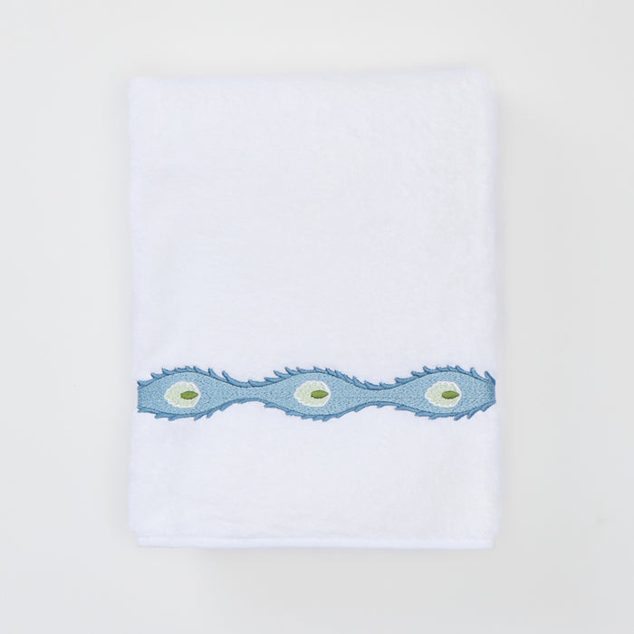 Folded white bath towel with a light blue wavy embroidered trim featuring green oval motifs.