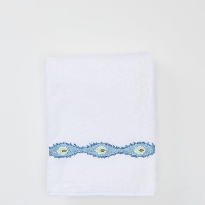 Folded white bath towel with a light blue wavy embroidered trim featuring green oval motifs.