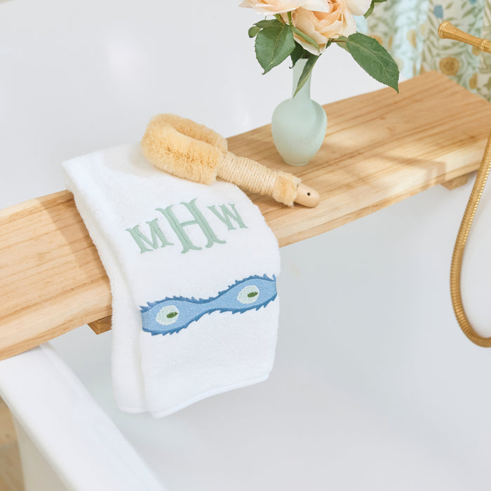 White Weezie hand towel with a green monogram and blue Lee Jofa embroidery on a wood caddy.