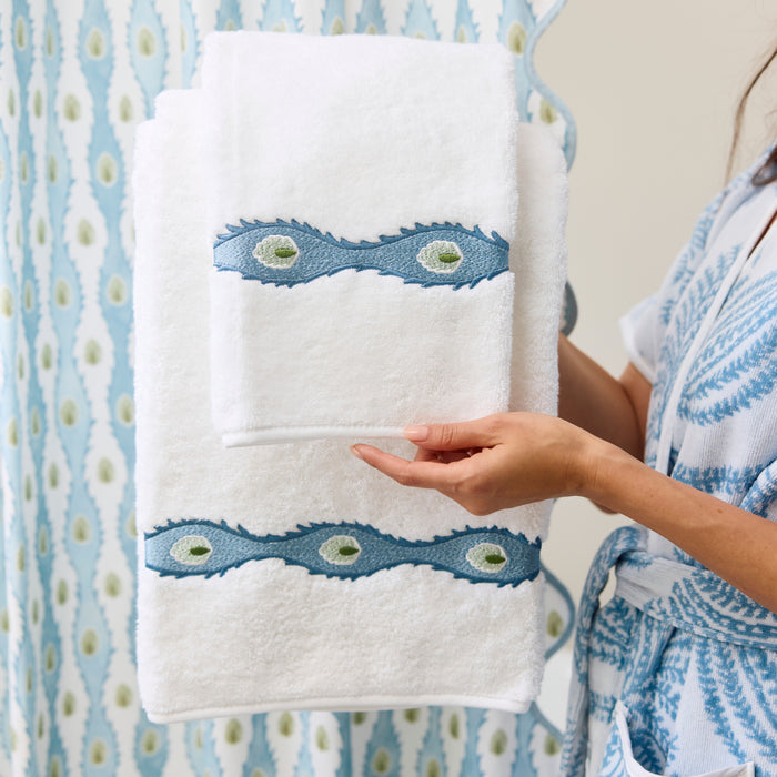 Monogrammed Weezie towel with blue floral embroidery on a caddy next to a bath brush and roses.