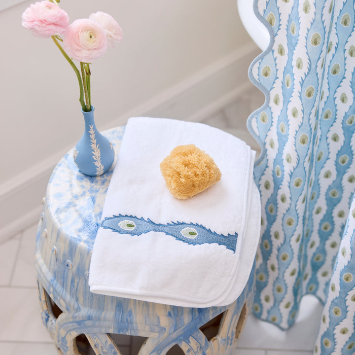 White Weezie towel with blue Lee Jofa embroidery draped on a blue stool next to pink flowers.