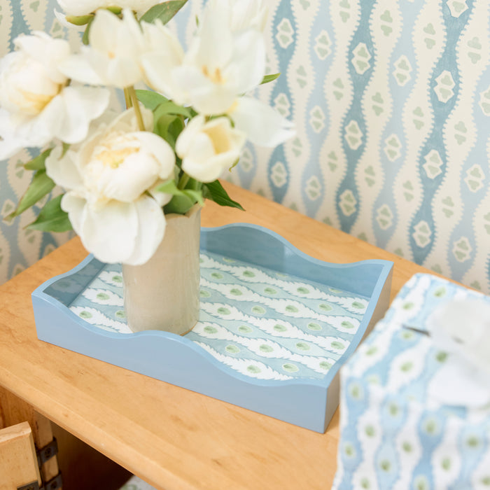 Light blue lacquer tray with floral pattern holding a vase of white flowers on a wooden table.