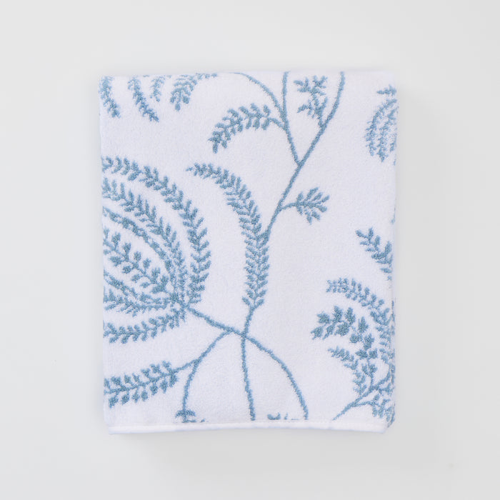 A folded white bath towel featuring a delicate light blue Palmero botanical pattern