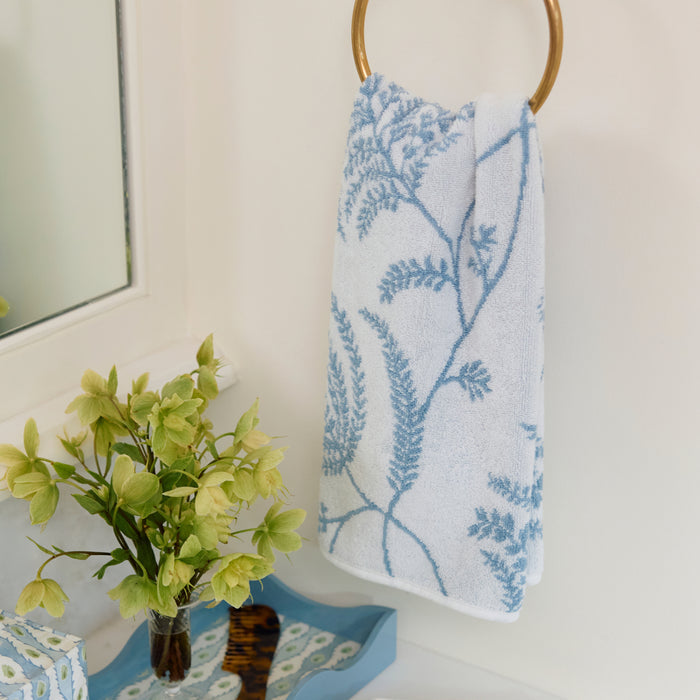 White hand towel with light blue Palmero floral pattern hanging on a brass towel ring.