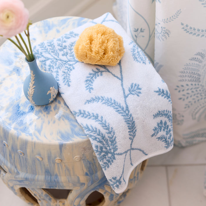 Palmero sky botanical towel draped on a ceramic stool with a blue vase and sea sponge.