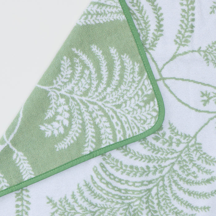 Close-up of a white hand towel featuring a sage Palmero botanical pattern and green piped edge.