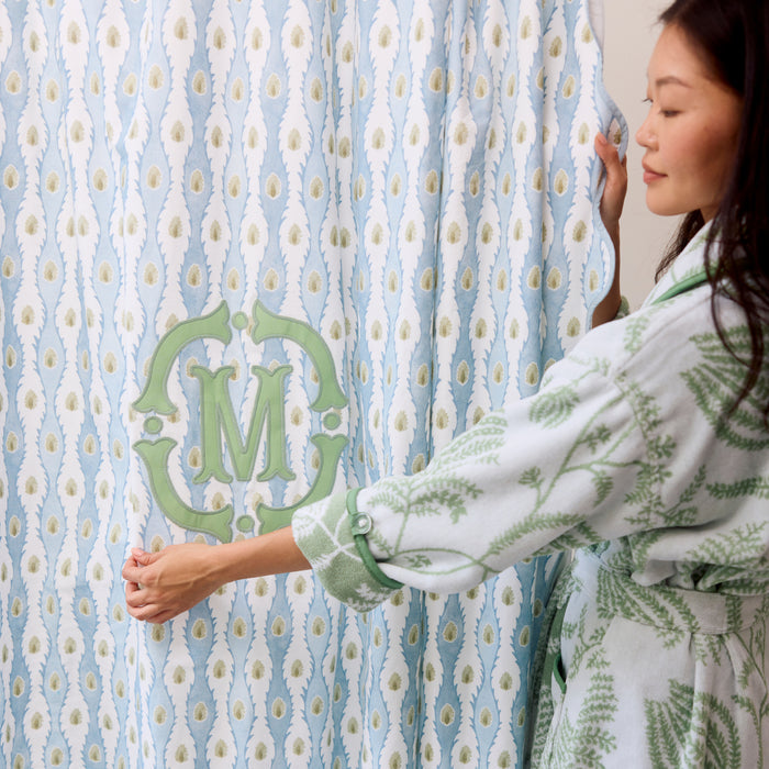 Woman in robe holding a monogrammed Lee Jofa Marciana blue and white patterned shower curtain.
