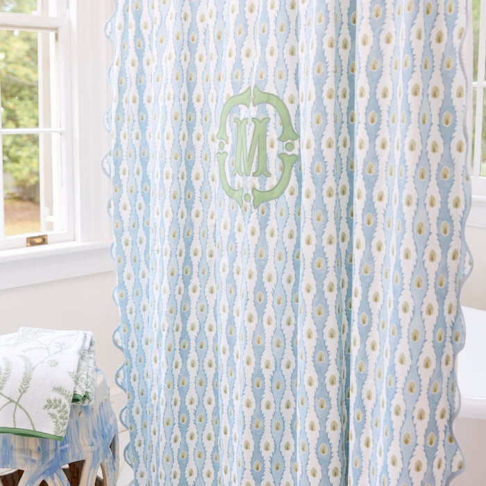 White and blue patterned shower curtain with a green M monogram and blue scalloped trim.