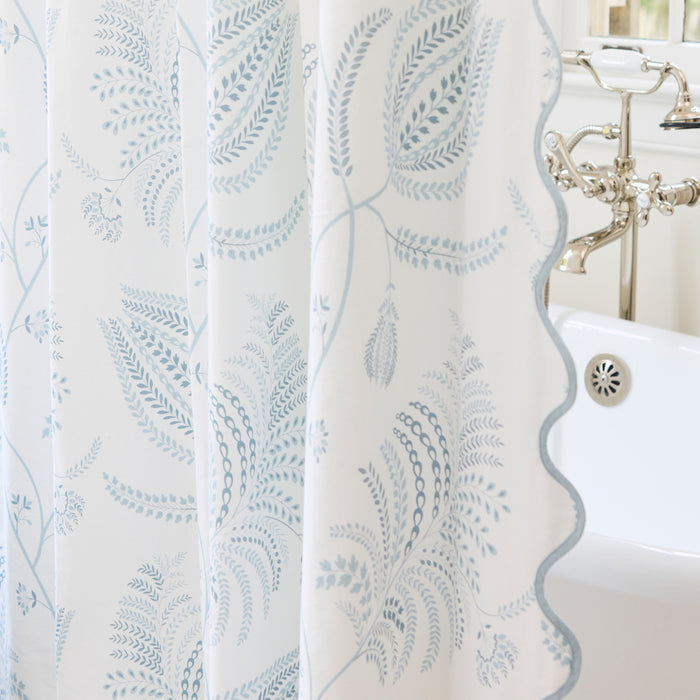 Detail of the Palmero Sky patterned shower curtain with light blue scalloped edge and tub.