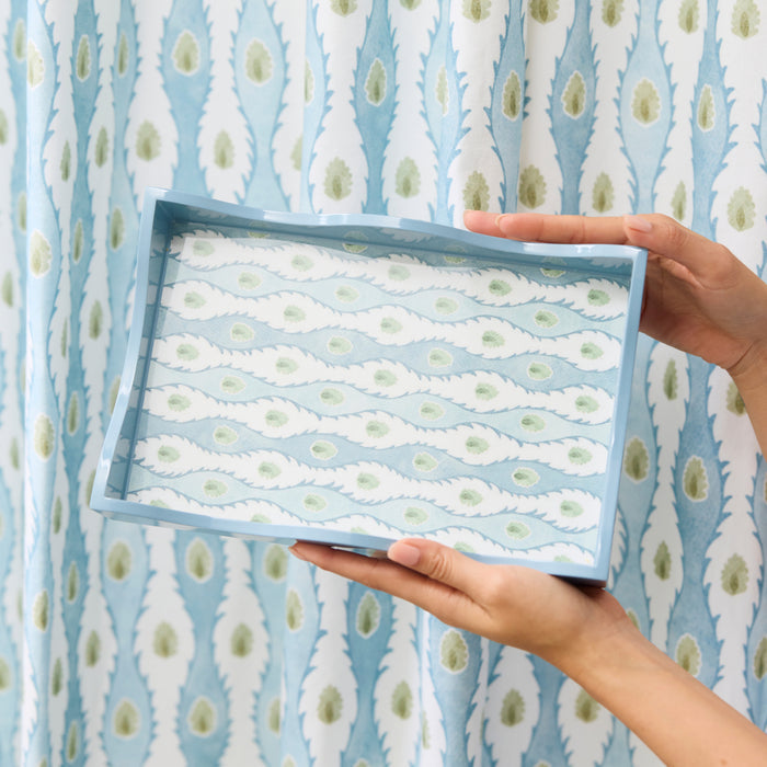 Hands holding a light blue lacquer tray featuring the blue and green Marciana pattern.