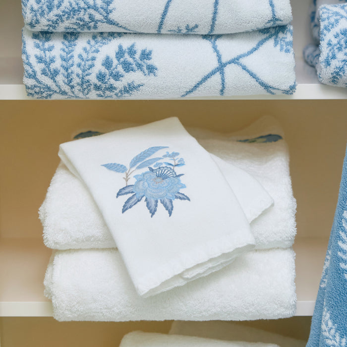 Stack of folded white Weezie towels featuring light blue floral embroidery on a shelf.