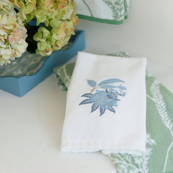 White powder towel with blue floral embroidery folded on a green towel next to a blue tray.