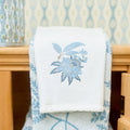 A white Weezie bath towel with blue Davenport floral embroidery hangs on a brass ring.