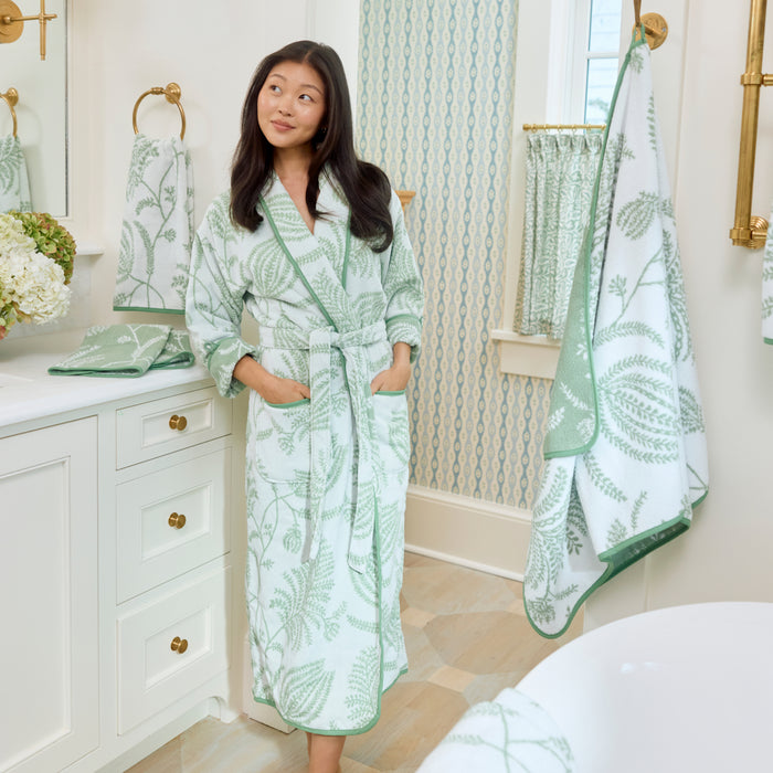 Smiling woman modeling a sage green and white patterned long plush robe with hands in pockets.