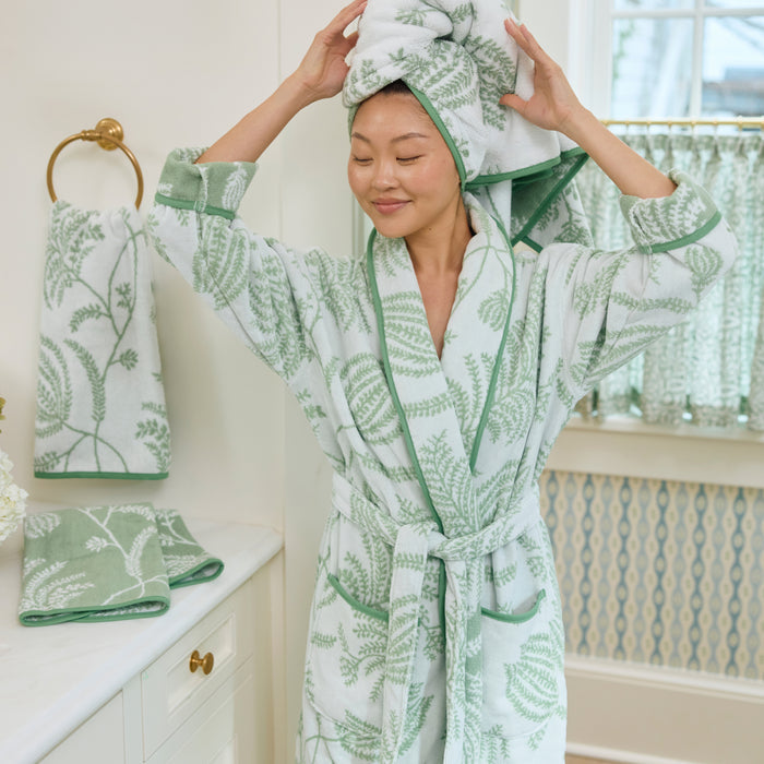 Woman wearing a long plush robe in a sage green and white floral print with green piped edges.