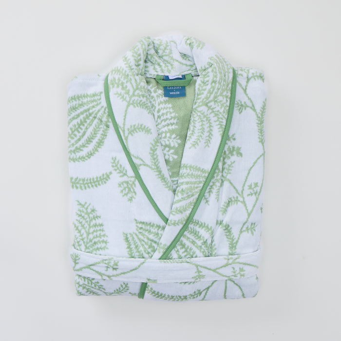 Folded white plush robe featuring a sage green botanical pattern and green piped edges.