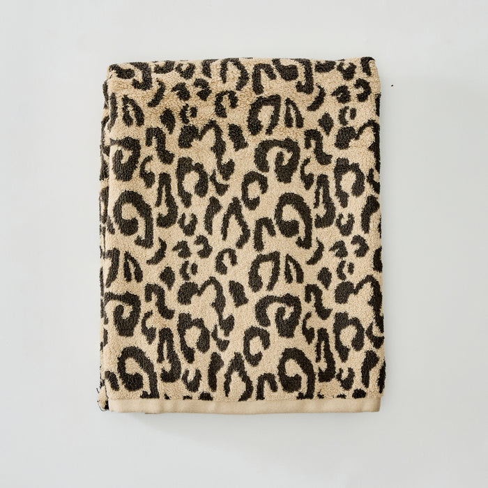 A folded plush towel with a classic leopard print pattern in beige and black, displayed flat against a light gray background.