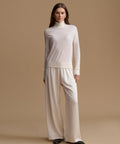 A woman modeling a cream-colored knit turtleneck sweater and matching wide-leg trousers against a solid beige studio background.